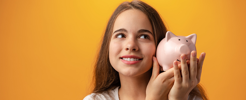 Teen girl with piggy bank on yellow background